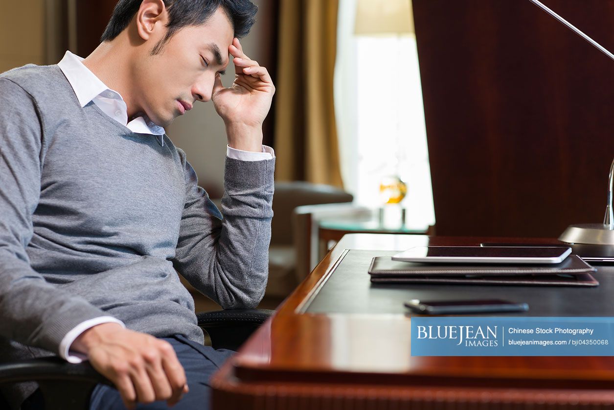 Tired Chinese businessman sitting in study