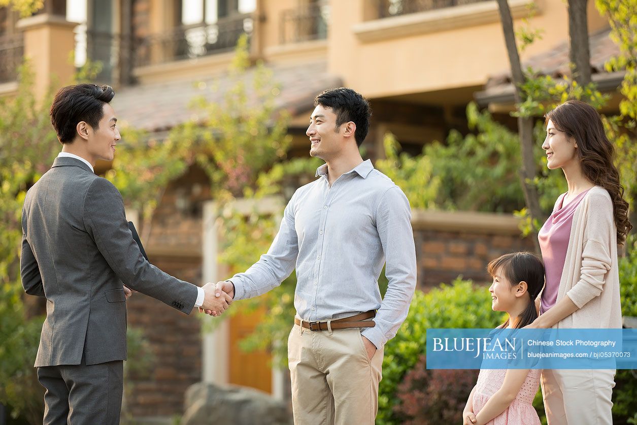 Happy young Chinese family shaking hands with realtor