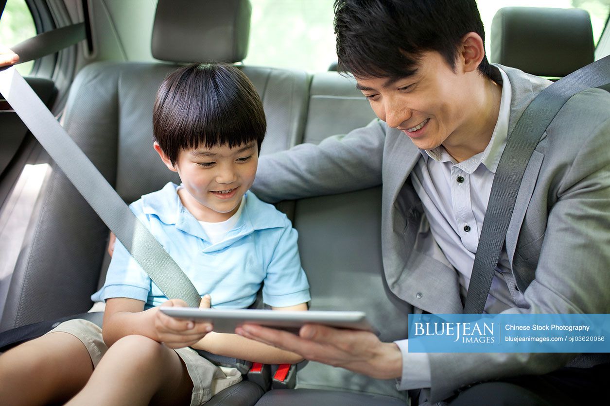 Happy Chinese father and son with digital tablet in car