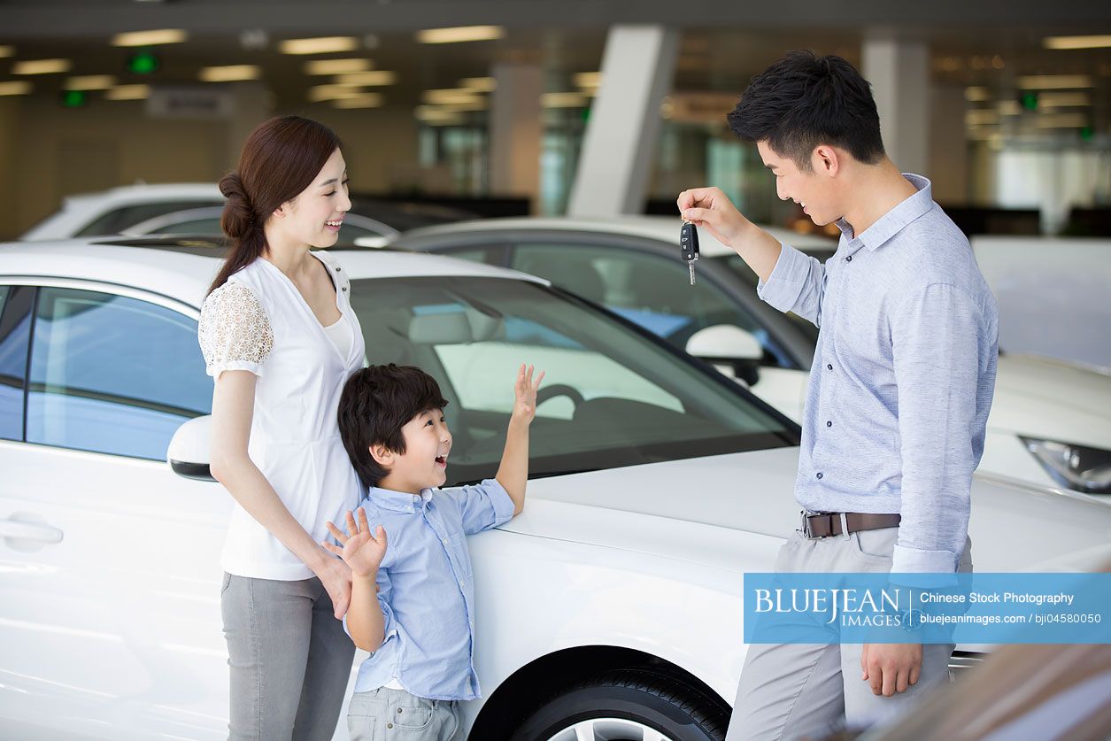 Young Chinese family buying car in showroom