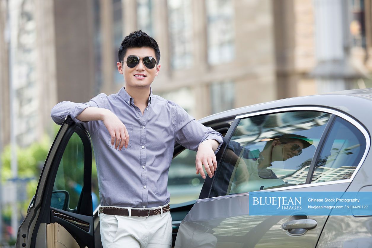 Young Chinese man standing next to his car