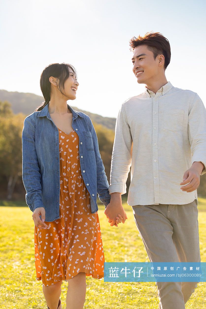 快乐的年轻情侣手牵手在草地上散步