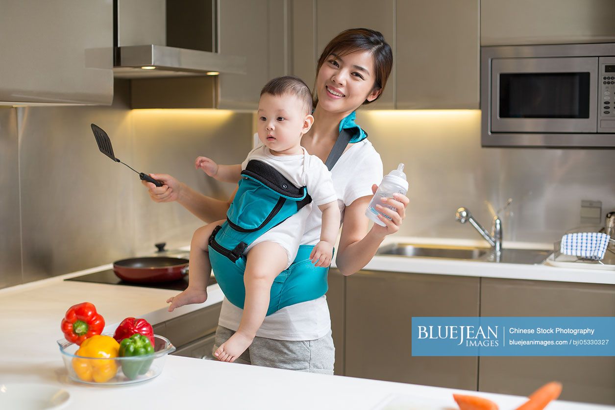 Chinese mother holding baby and cooking in the kitchen