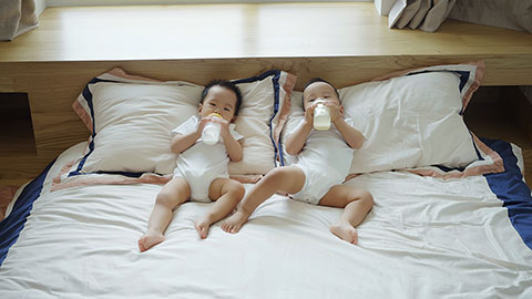 Two twin babies drinking formula from bottles.