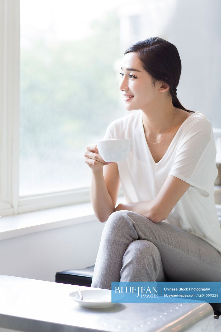 Happy young Chinese woman drinking coffee in coffee shop