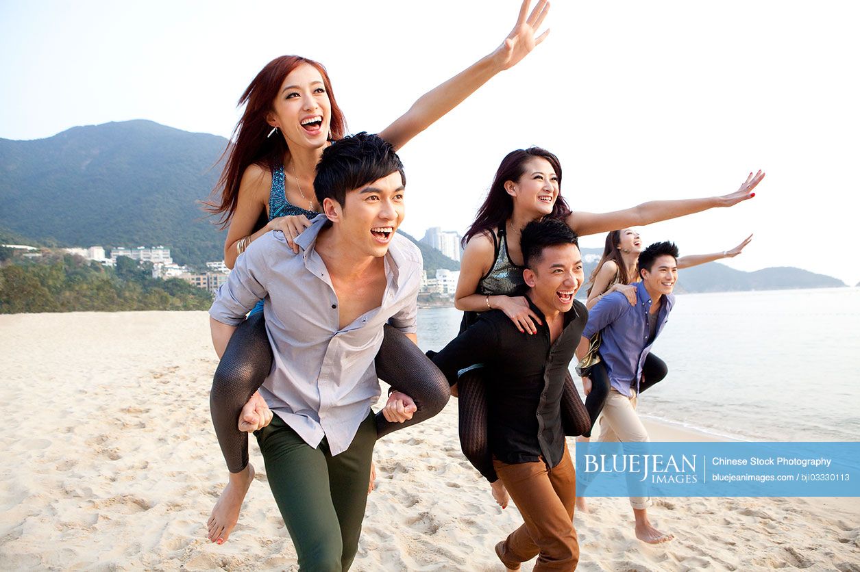 Excited young Chinese people playing piggyback on the beach of Repulse Bay, Hong Kong
