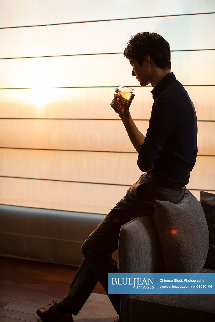 Young Chinese businessman drinking alcohol in hotel room