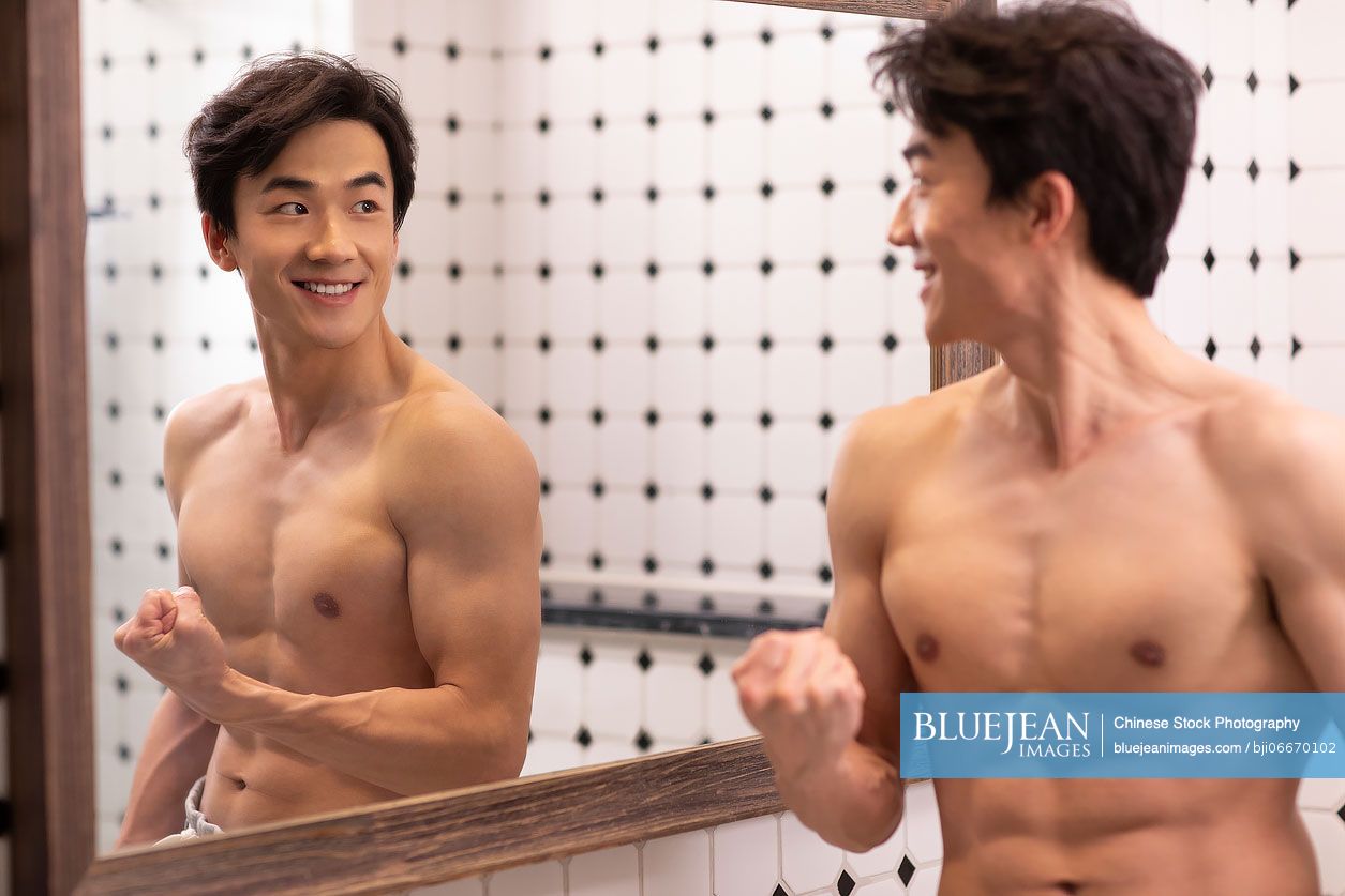 Young Chinese man showing muscles in front of a mirror