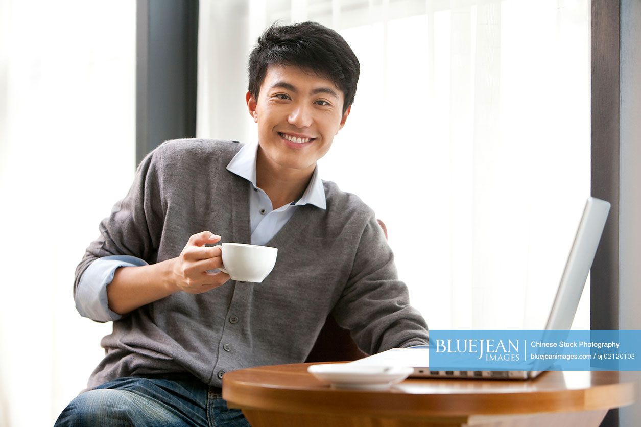 A young Chinese man smiling and holding a cup of coffee