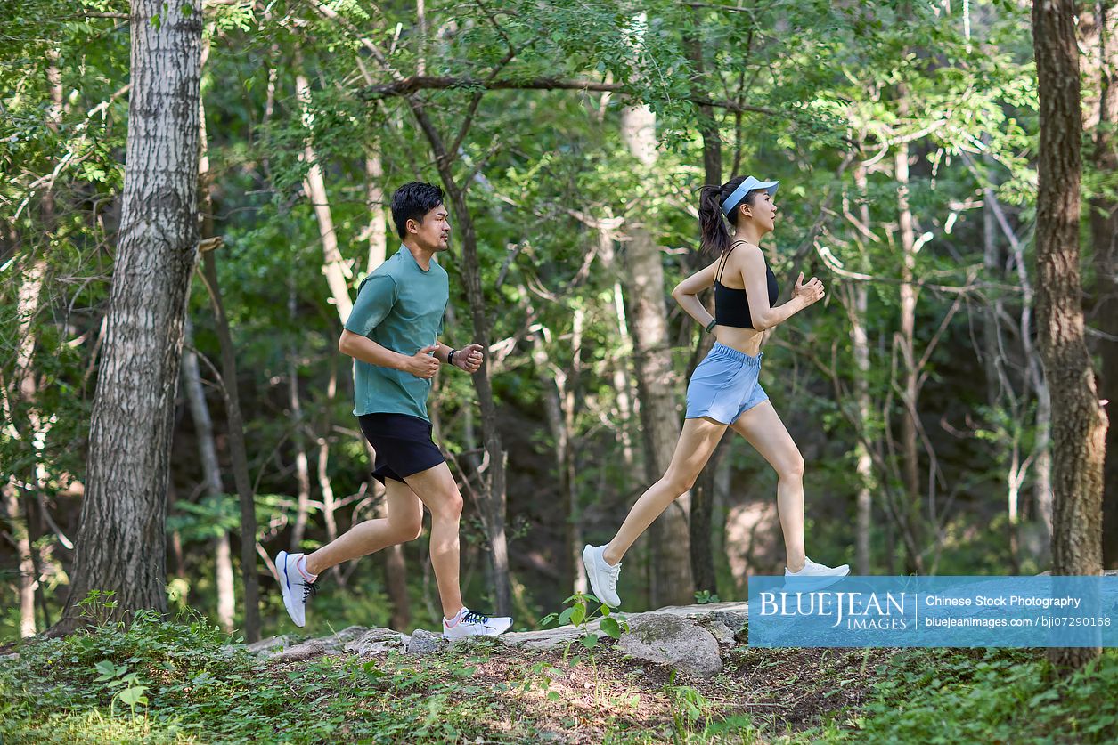 Young couple jogging along a road surrounded by lush trees