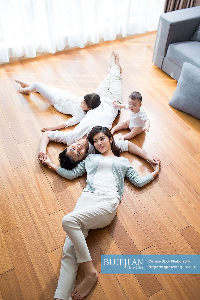 Happy young Chinese family resting on wooden floor