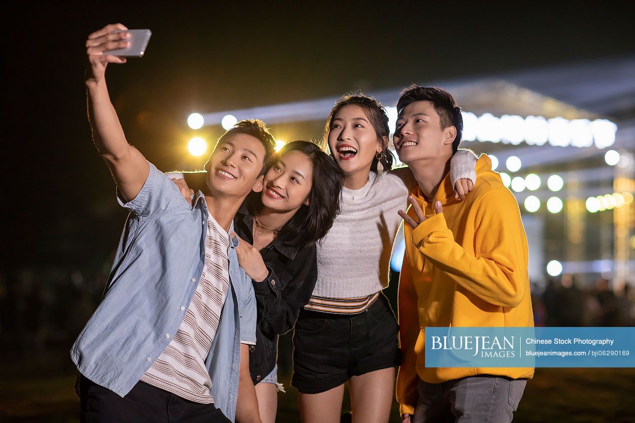 Happy young Chinese friends taking selfie at music festival